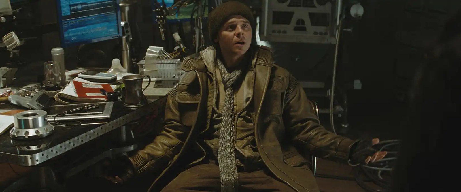 Simon Pegg as Scotty in Star Trek (2009) spreads his arms in a questioning gesture, sitting in warm clothing at a cluttered desk. 