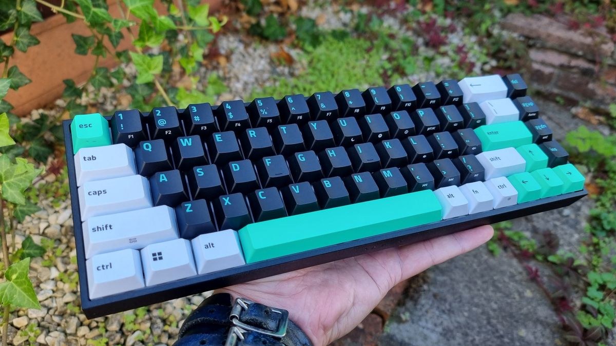 The Razer Reclusa X Mini 65% gaming keyboard held in the hand outside, in front of some foliage