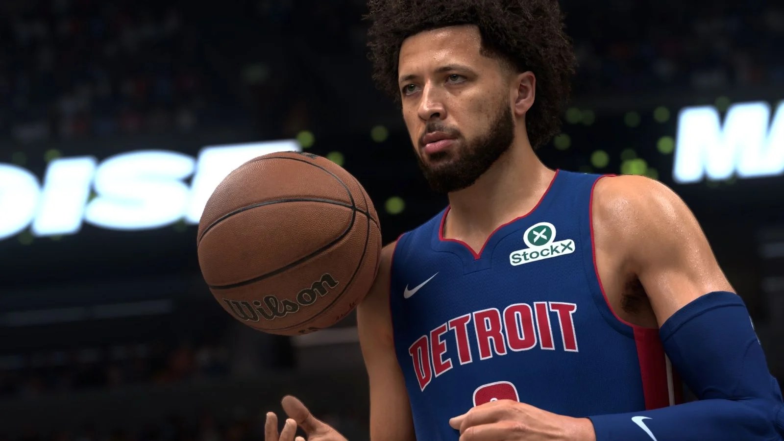 A basketballer in a navy blue jersey and with a mid-sized afro and short, neat beard tosses a ball up casually from their hand.