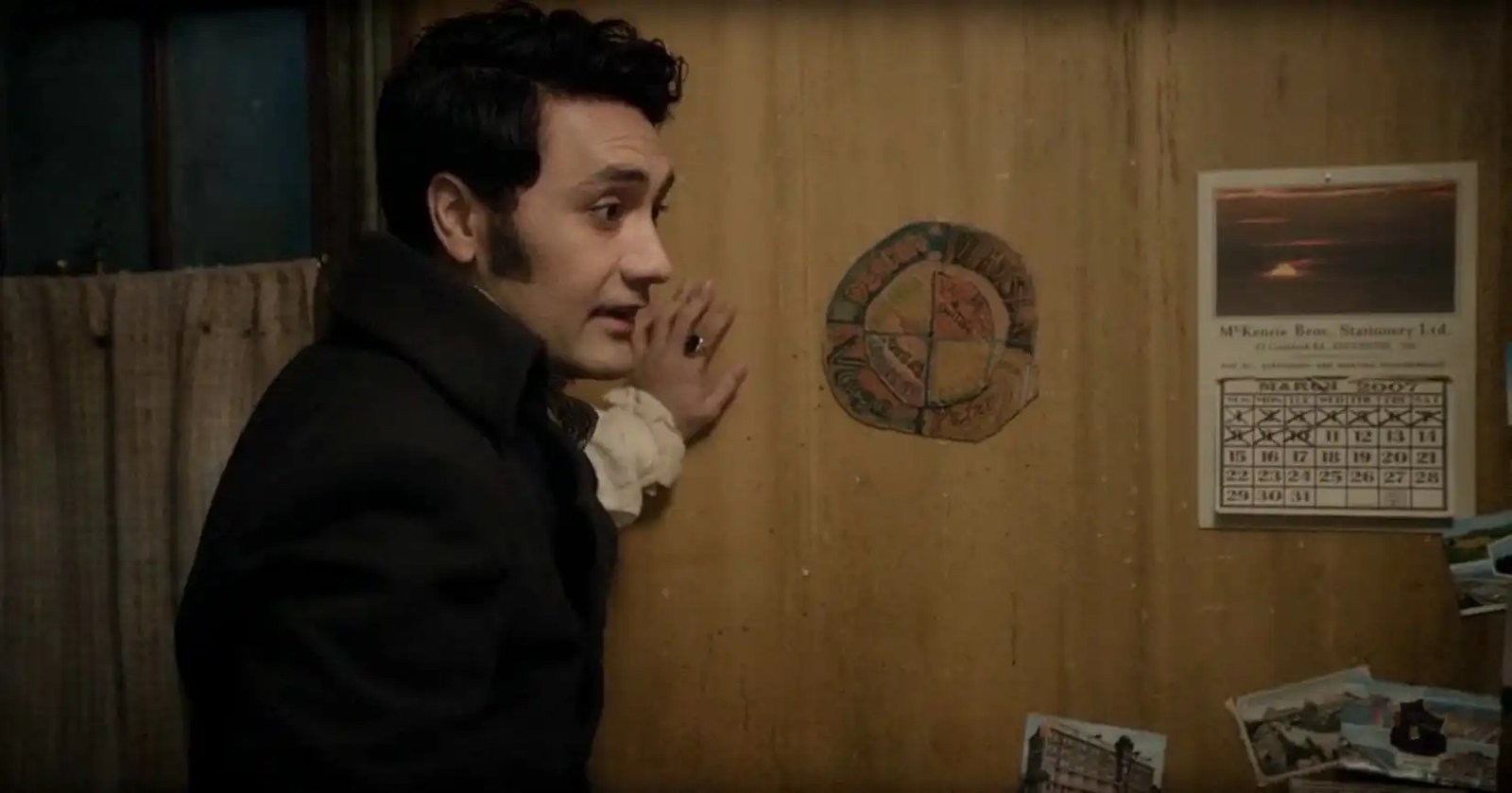 Taika Watiti leans against a wall looking at a calendar in What We Do in the Shadows